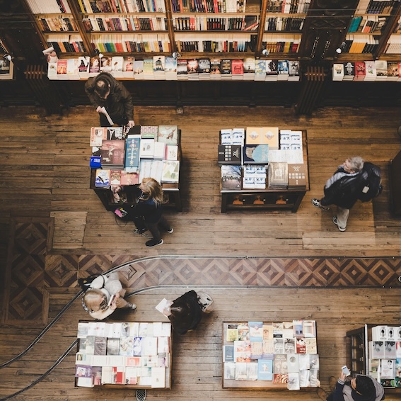 Vista cenital de una librería: mesas con novedades, estanterías repletas y gente ojeando libros
