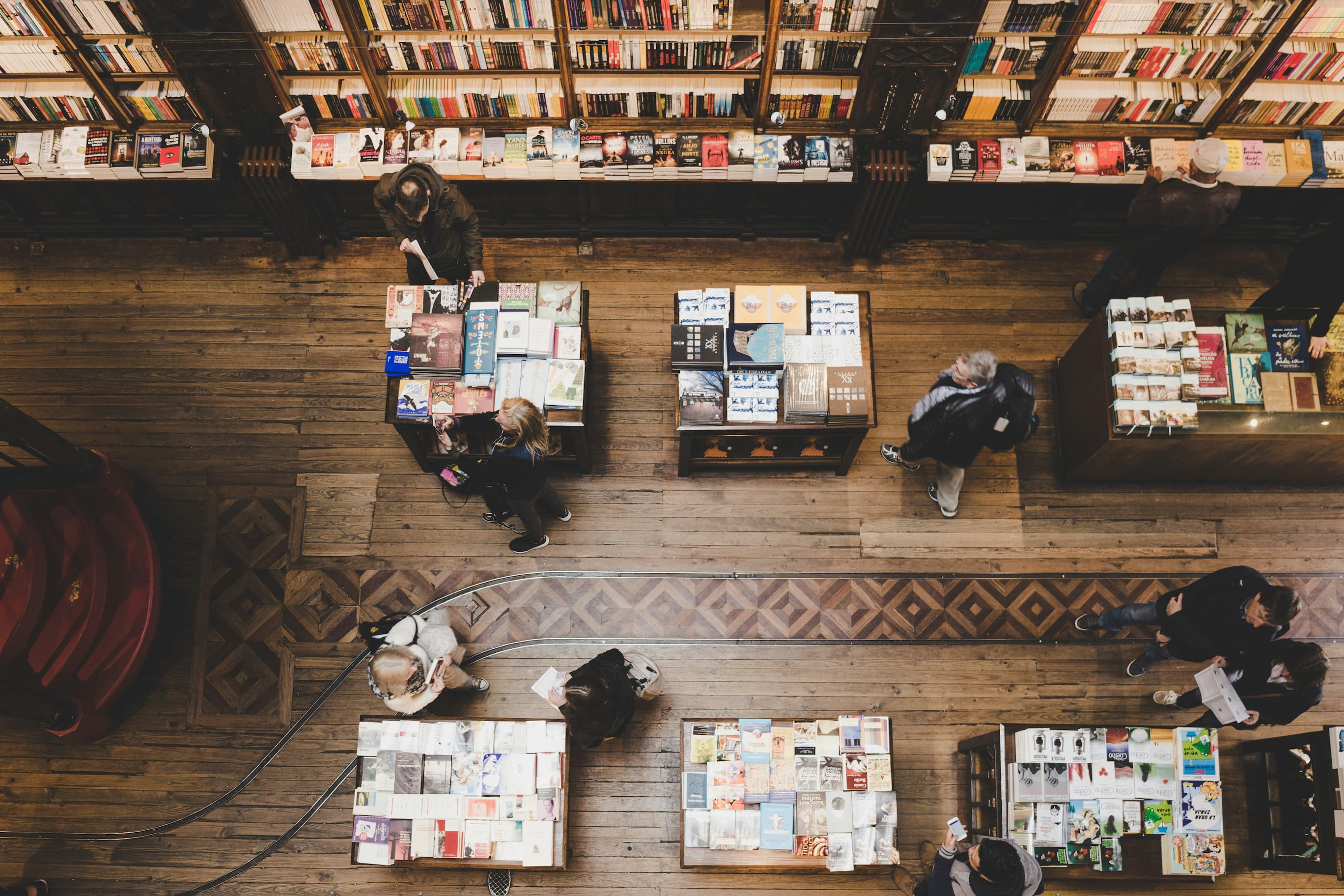 Vista cenital de una librería: mesas con novedades, estanterías repletas y gente ojeando libros
